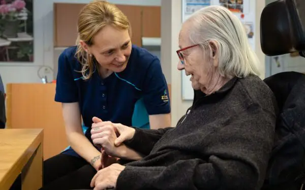Verpleegkundige naast een vrouw in de rolstoel die haard hand vasthoudt